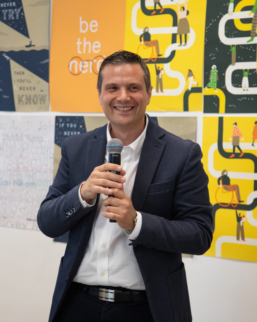 Foto del presidente di Fondazione Italia digitale Francesco di Costanzo, sorridente con microfono. Sullo sfondo un manifesto colorato giallo nero