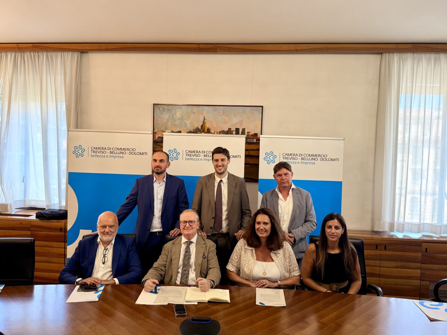 Il Presidente-con- i-Componenti-di Giunta seduti e in pedi in sala giiunta dietro i roll up con il logo camerale azzurro
